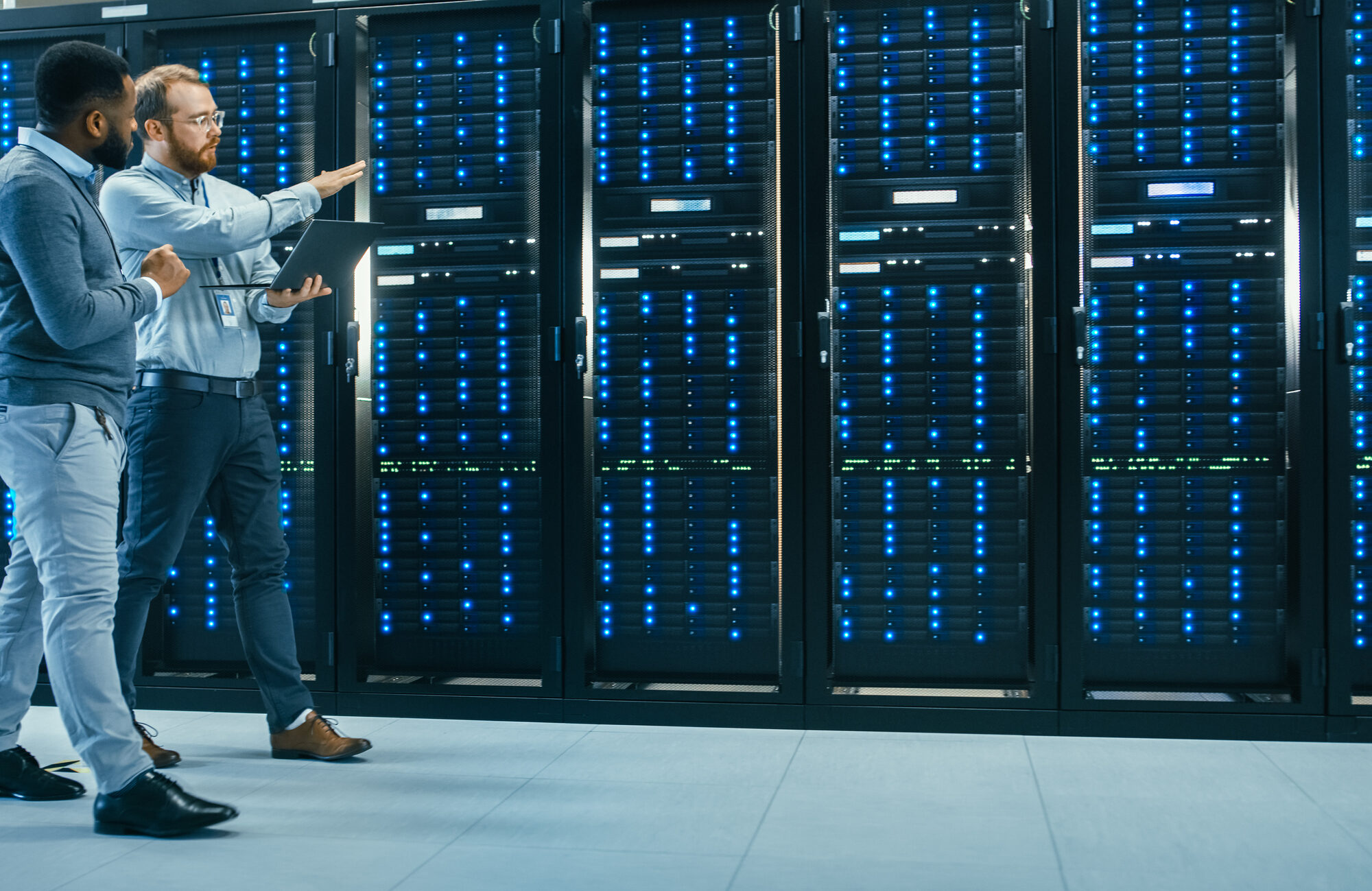 Two data center technicians walking past illuminated server racks.